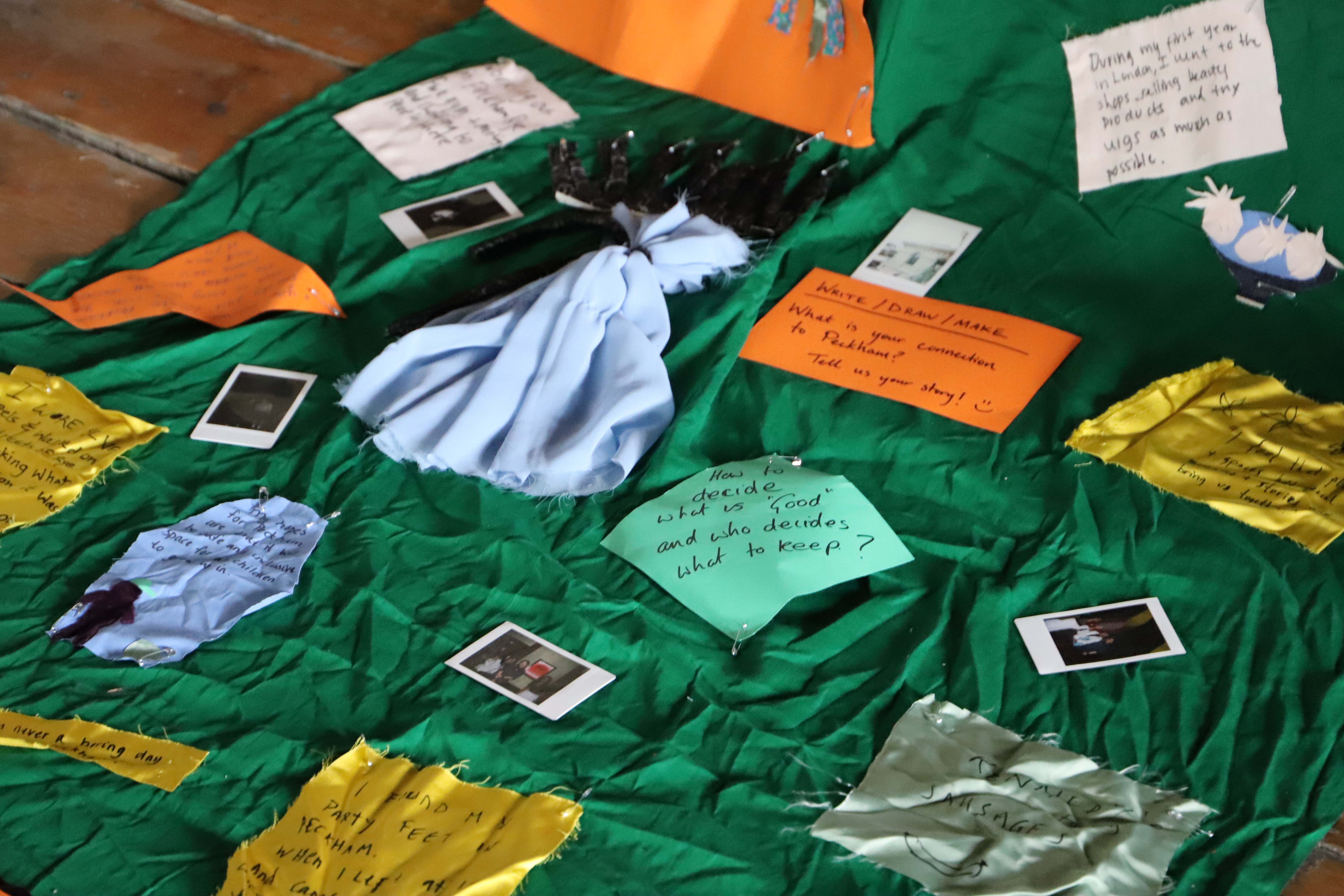 Chiara and Abbey sitting on the floor of the Old Waiting Room in Peckham, together with the workshop participants. On the floor in front of them crafts material.