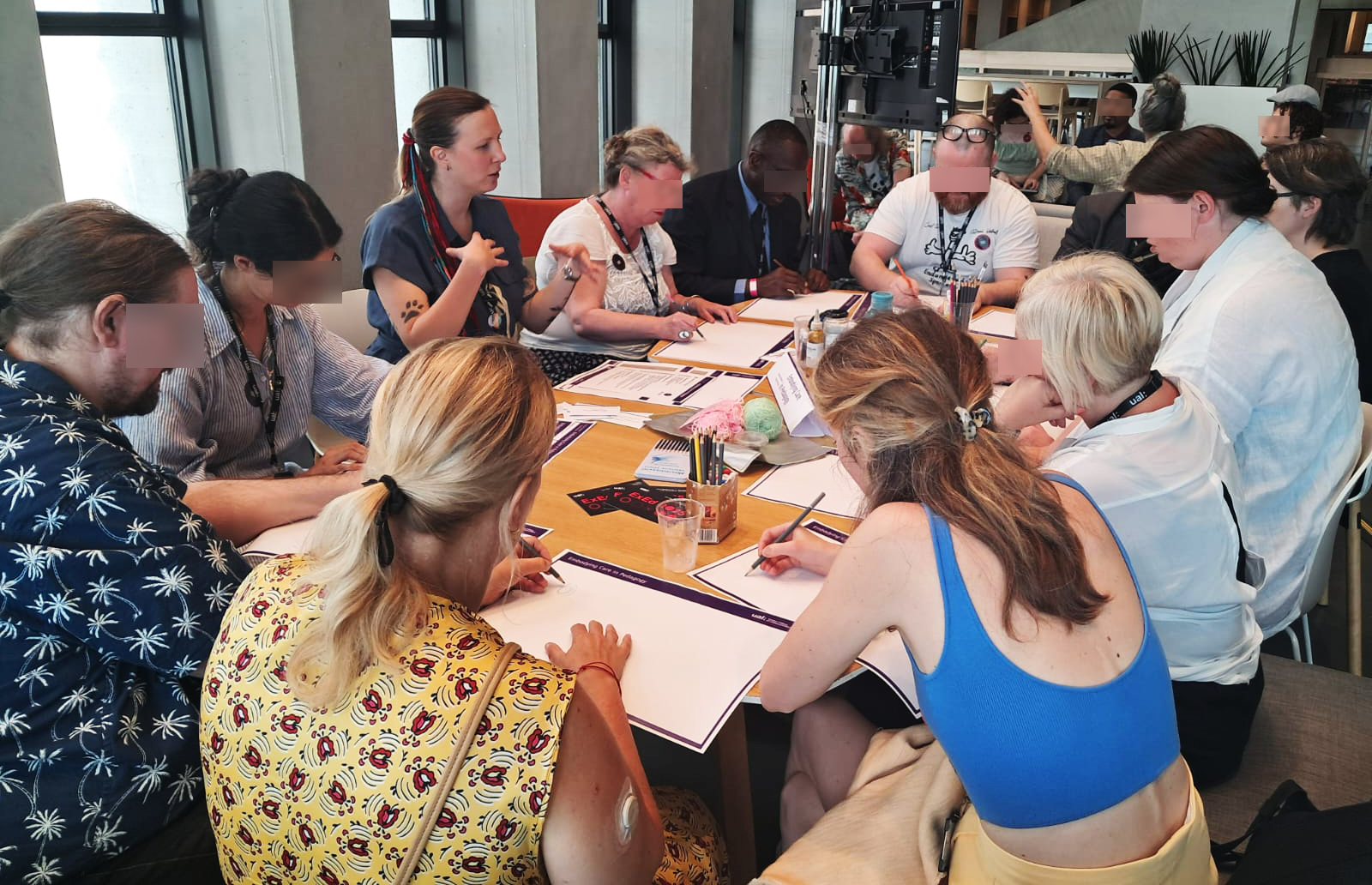 Chiara and a group of people with crafts materials are sitting around a table. They are working on body mapping.