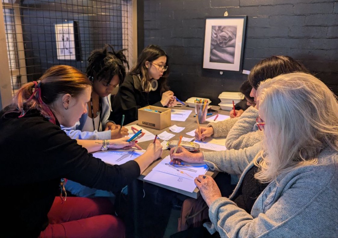 A group of changemakers are sitting at a table. They are focused on drawing on some papers which display body-like shapes.
