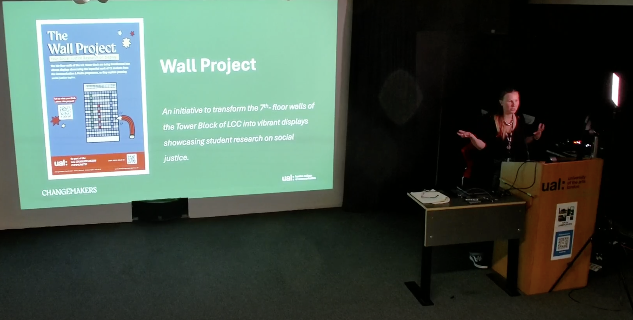 Chiara presenting on a stage with a screen presenting a slide titled Wall Project